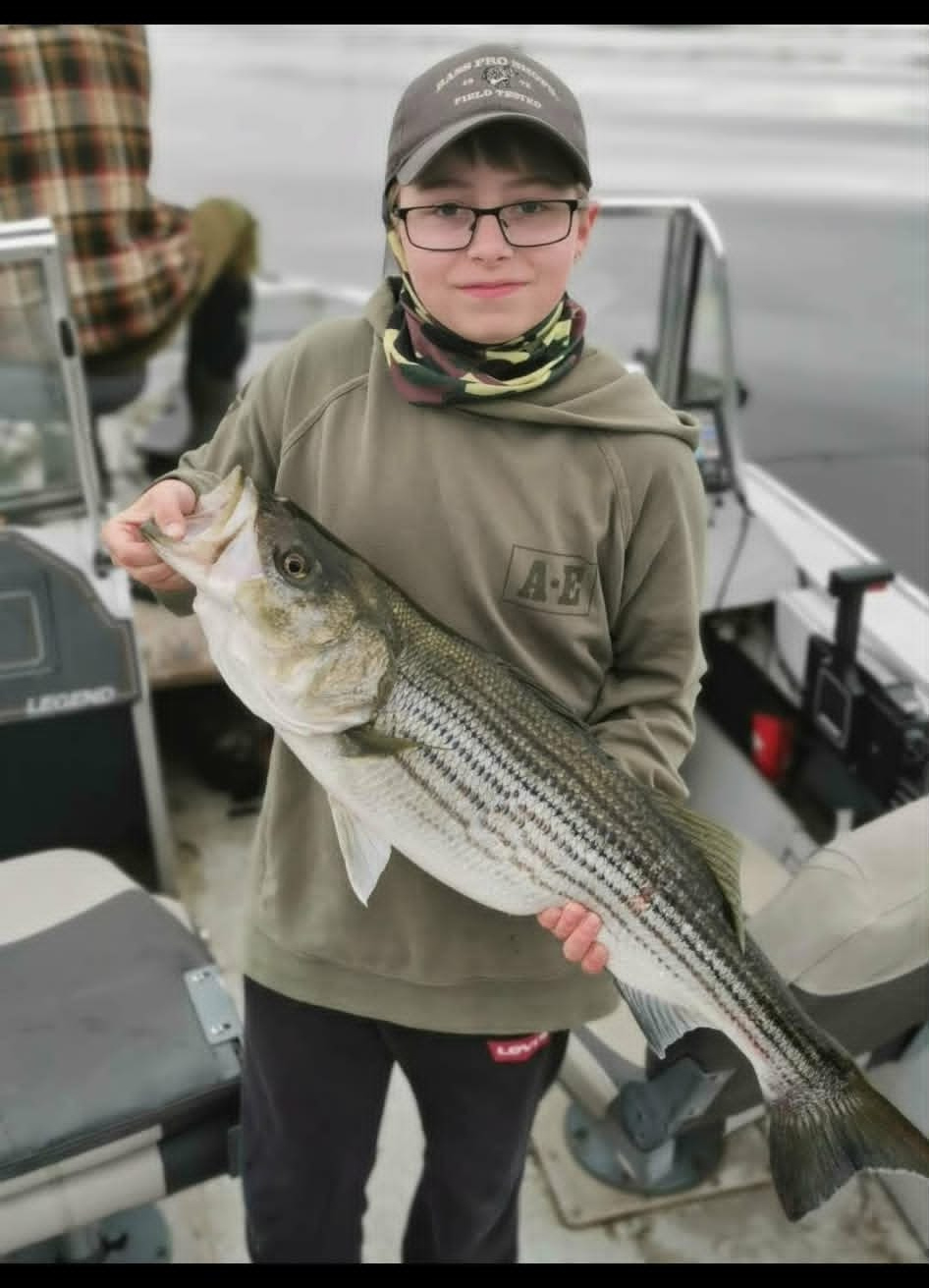 Young angler holding a striped bass on the boat