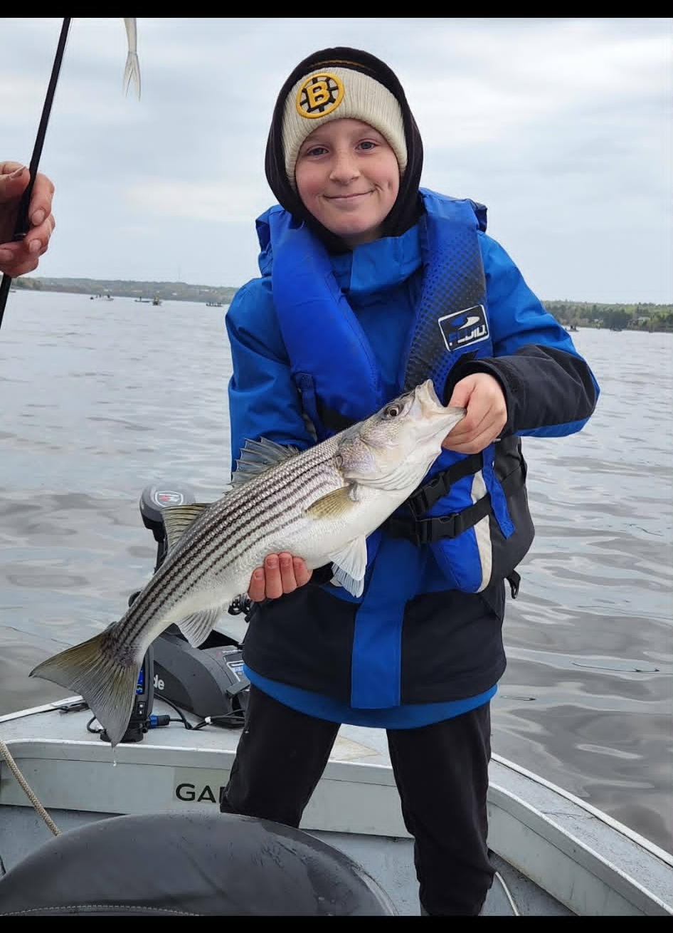 Young angler holding a striped bass on the boat