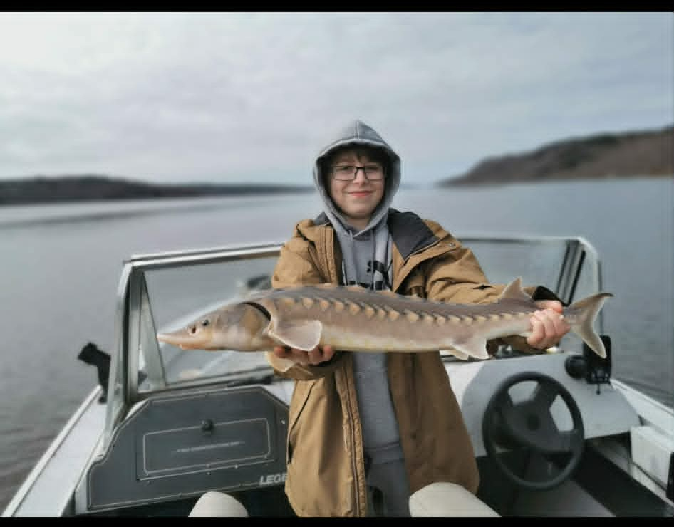 Young angler holding a sturgeon on the boat